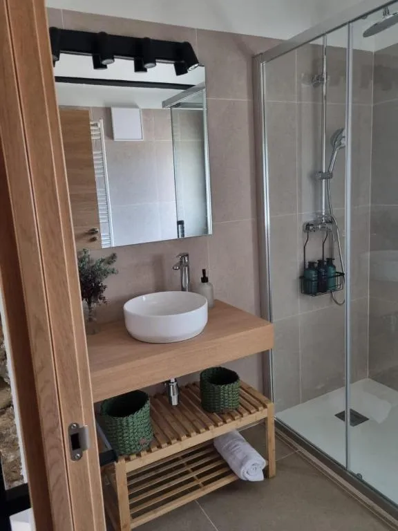 Lavabo blanc sobre moble de fusta amb cistelles de vímet i dutxa de vidre al costat