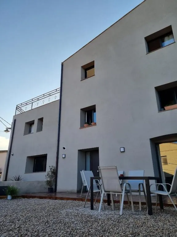 La casa vista des del pati interior de grava, amb la taula exterior i el cel blau