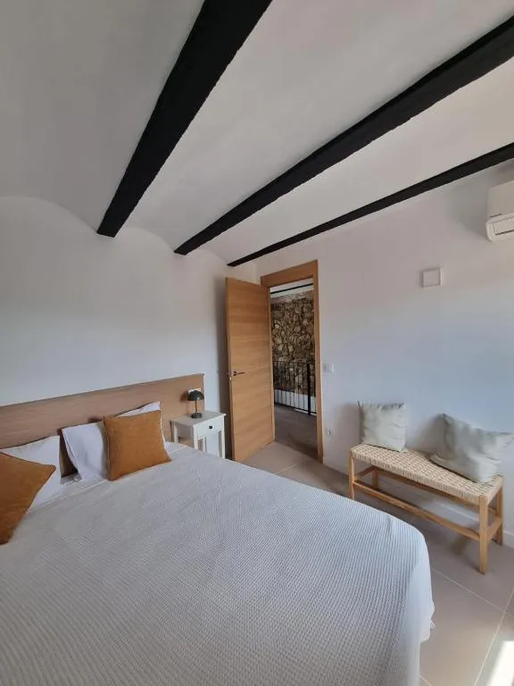 Habitació doble amb llit de matrimoni, coixins ocre i bigues d’acer negre al sostre