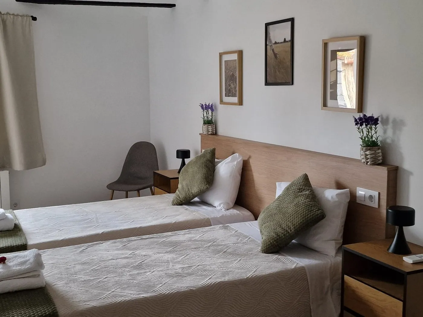 Habitació amb dos llits individuals ajuntats, coixins de vellut verd oliva i làmines emmarcades sobre la capçalera de fusta