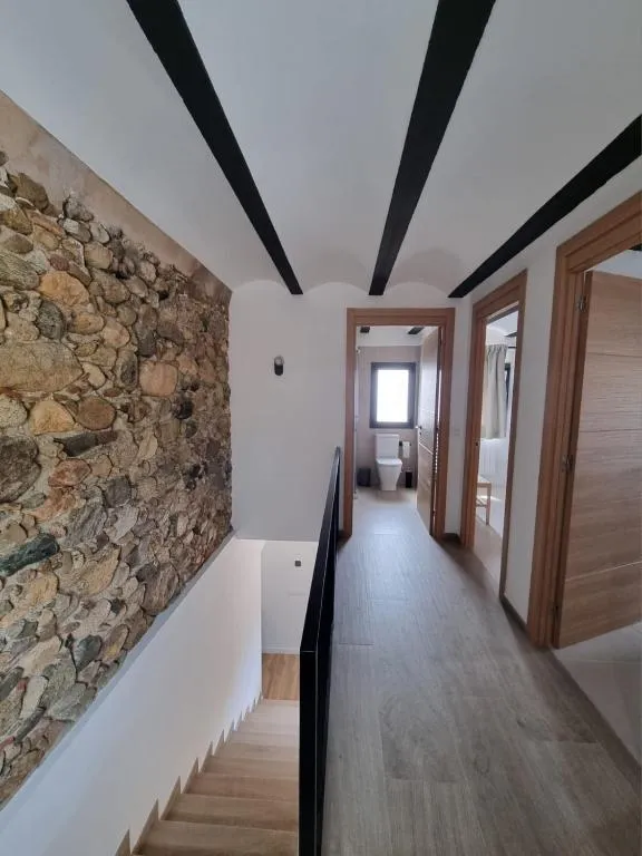 Passadís de la planta superior amb mur de pedra seca i bigues d’acer negre al sostre