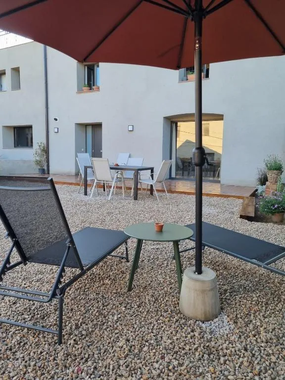 El pati privat de Les Ametlles amb el para-sol obert, la taula per menjar a fora i la façana de la casa al fons