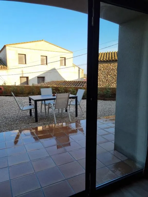 El pati vist des de dins de la casa a través de la porta de vidre, amb la taula parada