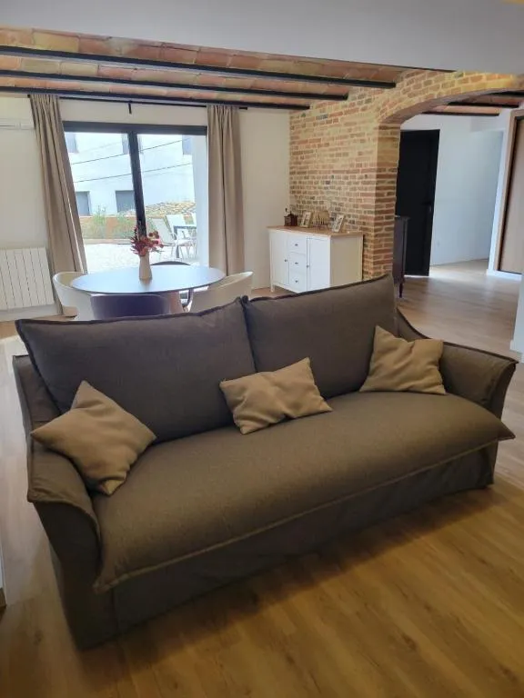 Sofà gran de la sala sota l’arc de maó vist, amb el menjador i la porta al pati al fons
